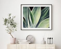 an art print hangs on the wall above a dresser with books, plants and vases