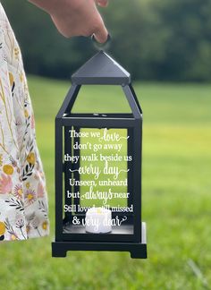 a person holding a small lantern with a poem on it in front of a grassy field