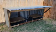 a couple of beds sitting inside of a metal structure on top of grass next to a wooden fence