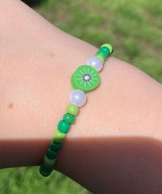 a close up of a person wearing a green bracelet with beads and a kiwi on it