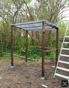 a wooden structure sitting in the middle of a field next to a ladder and trees