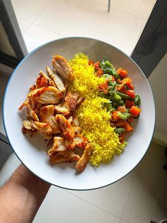 a white plate topped with chicken, rice and veggies next to a window