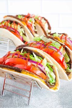 three tacos with tomatoes, lettuce and tomato on them sitting on a rack