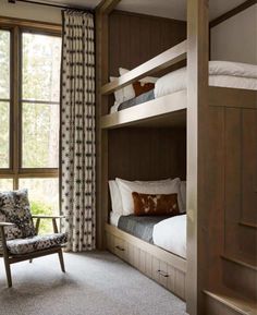 a bedroom with bunk beds and chairs next to a window that looks out onto the woods