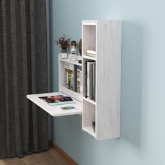 a white book shelf with books and magazines on it in front of a blue wall