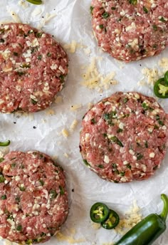 three hamburger patties sitting on top of white paper next to green peppers and jalapenos