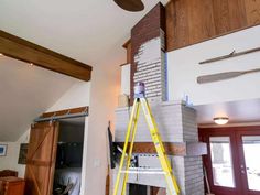 a man standing on a ladder in front of a fire place with a ceiling fan