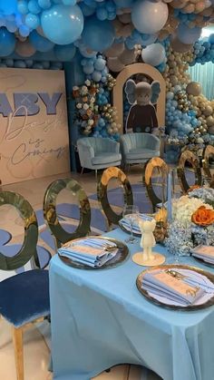 a table set up for a baby shower with blue and gold decorations, balloons and plates