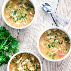 three bowls filled with soup on top of a wooden table next to some parsley