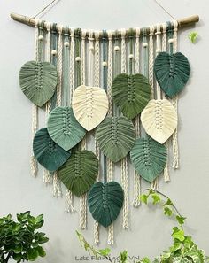 a green and white wall hanging with leaf shapes on it, next to a potted plant