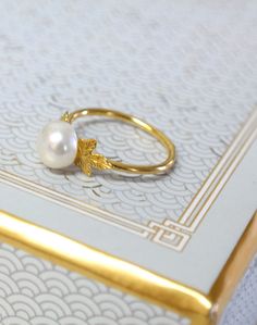 a pearl ring sitting on top of a white and gold book with an ornate border around it