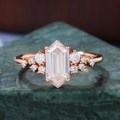 a ring with an emerald cut diamond surrounded by small white diamonds on a green marble surface