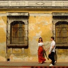 a man and woman walking down the street in front of an old building with barred windows