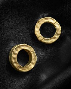 two pairs of gold earrings sitting on top of a black leather bag, one with an oval