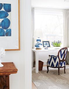 a blue and white chair sitting in front of a window next to a table with pictures on it