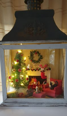 a small christmas tree in a glass box with lights on it and presents under the window