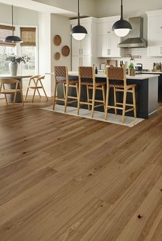 a kitchen filled with wooden floors and chairs next to an island counter top under two pendant lights