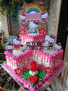 a hello kitty birthday cake with pink icing and rainbows on the top tier