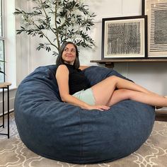 a woman sitting on a bean bag chair in a living room with a potted plant