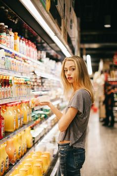 a woman is standing in front of a grocery aisle and looking at orange juice on the shelf