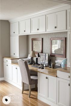 a home office with white cabinets and wood flooring is pictured in this image, there are two framed pictures on the desk