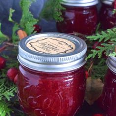 two jars filled with red liquid sitting on top of a table next to green leaves