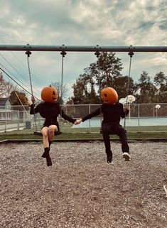 two people in halloween costumes are swinging on swings with pumpkin faces painted on their heads