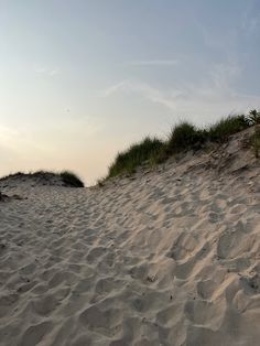 there is sand dunes with grass growing on the top and one in the distance, against a blue sky