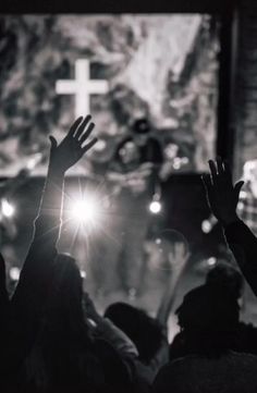 people raising their hands in front of a cross with the words god, we trust