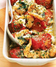 a casserole dish with shrimp, tomatoes and feta cheese in it on a wooden table