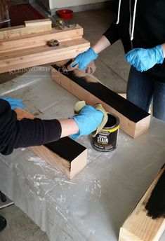 two women in blue gloves are working on some wooden pieces with paint and sandpaper