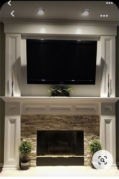 a flat screen tv mounted above a fireplace with potted plants on the mantel