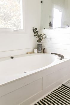 a white bath tub sitting next to a bathroom sink under a large mirror on the wall