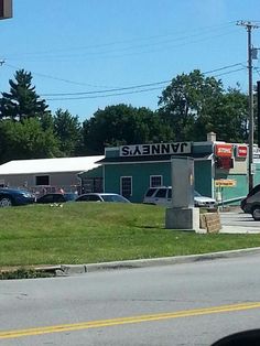 a gas station sitting on the side of a road next to a green field with cars parked in front of it