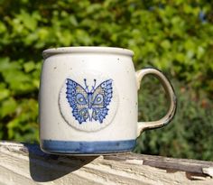 a blue and white coffee cup sitting on top of a wooden table next to trees