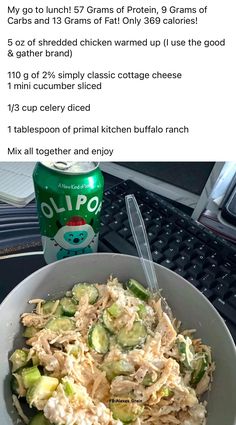 a white bowl filled with salad next to a can of soda on top of a computer desk