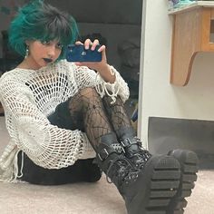 a woman with green hair sitting on the floor taking a selfie in front of a mirror