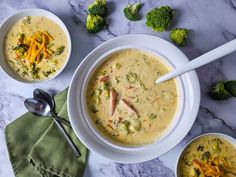 two bowls of broccoli cheese soup on a marble countertop with spoons