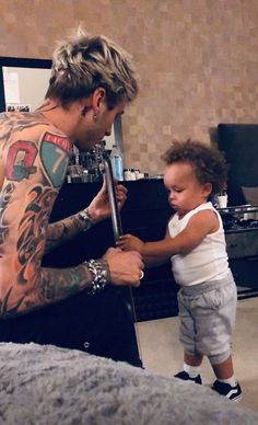 a man holding a baby while standing in front of a mirror with tattoos on his arms