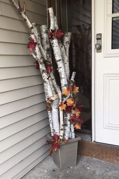 a metal planter filled with autumn leaves next to a white door and front entrance