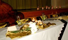 there are many candles on the table with gold cloths and flowers in front of them