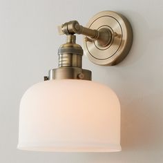 a light fixture on the wall with a white glass shade hanging from it's side