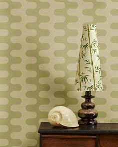 a lamp sitting on top of a wooden dresser next to a wallpapered wall