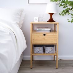 a nightstand with two baskets on it next to a bed and a plant in the corner