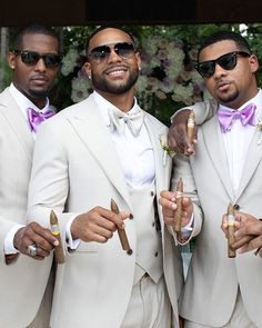 three men in white suits holding cigars and wearing sunglasses are posing for the camera