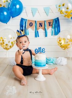 a baby sitting on the floor with a cake in front of him and some balloons