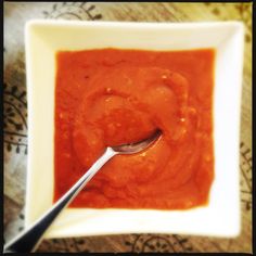 a spoon sitting in a bowl filled with red sauce on top of a tablecloth