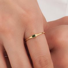 a woman's hand wearing a gold ring with a green tourmaline stone