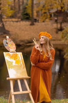 a woman standing next to an easel holding a paintbrush