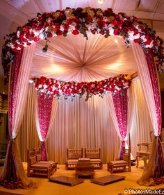 a wedding stage decorated with red flowers and white draping for the bride's ceremony